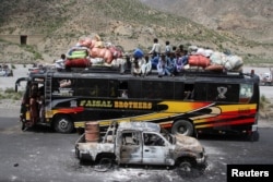 A bus with passengers sitting on the roof drives past a damaged vehicle, the day after separatist militants conducted deadly attacks in the Bolan district of Balochistan.